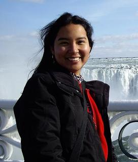 Mulher olhando para a frente sorrindo, em frente a uma paisagem de queda d'água